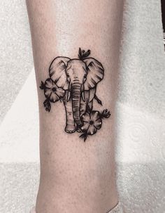 an elephant tattoo on the leg of a woman's legs with flowers around it