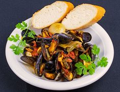 a white plate topped with mussels and bread on top of a black table