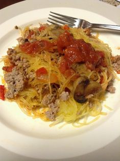 a white plate topped with spaghetti and meat covered in tomato sauce next to a fork