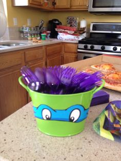 a green bucket filled with purple hair sitting on top of a counter next to a pizza