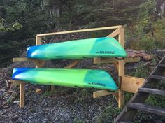 two blue and green surfboards are on a wooden rack near some stairs in the woods