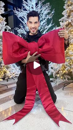 a man is holding up a red bow in front of white christmas trees with lights