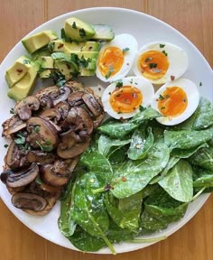 a white plate topped with mushrooms, lettuce and hard boiled eggs next to sliced avocado