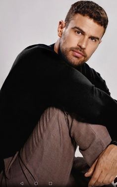 a man sitting on the ground with his arms crossed and looking at the camera while wearing a black hoodie