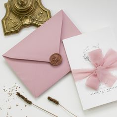 an envelope with a pink ribbon and a wax stamp on it next to some dried flowers