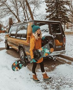 a woman walking in the snow with her snowboard next to an suv and trees