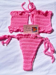 two pink crocheted bikinisuits with tags attached to them on a white sheet