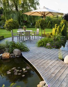 a wooden deck with an umbrella over it next to a small pond and patio furniture