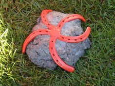 an orange plastic scissors laying on top of a rock in the grass with green grass around it