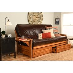 a brown leather futon sofa sitting on top of a hard wood floor next to a lamp