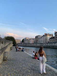 people are walking along the river bank near some buildings and water in front of them