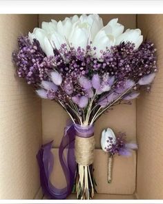 a bouquet of flowers in a box with purple ribbon around the bottom and white flowers on top