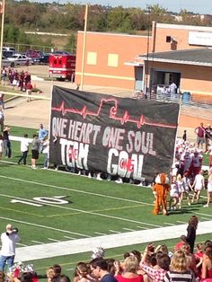 a group of people standing on top of a football field next to a banner that reads, we heart one soul ten o'clock