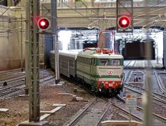 a green and white train traveling down tracks next to a red light at a station