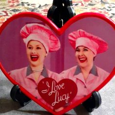 two women in pink hats holding up a heart shaped photo with the words i love lucy on it