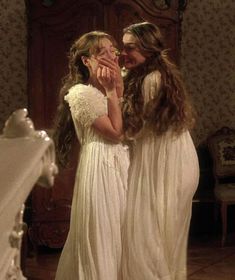 two women in white dresses standing next to each other with their hands on their faces