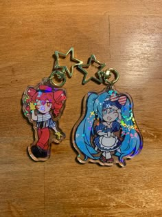 two keychains with cartoon characters on them sitting on a wooden table next to each other