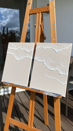 an easel sitting on top of a wooden floor next to a white painting board