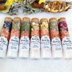 seven tubes filled with different types of herbs on a white surface next to dried flowers