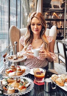 a woman sitting at a table holding a cup and plate with pastries on it