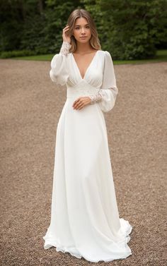 a woman in a white wedding dress standing on gravel road with trees in the background