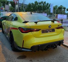 the rear end of a yellow sports car parked on the side of the road with other cars behind it