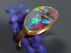 "It's a rainbow party on your finger! This ring has an absolutely gorgeous free form oval Australian Boulder Opal set in luscious 22K Gold. The ring has an 18K Royal Yellow Gold band which has a subtle hammered texture and the backplate is 14K Rose Gold which has a hand stamped stars and stardust. The whole ring has a soft brushed finish. The stone has electric magenta, blue, yellow, orange, and green color flashes with some chocolate brown host rock. Even in very low light there are a lot of br Adjustable Opal Ring With Large Stone, Luxury Gold Opal Ring With Cabochon, Gold Adjustable Opal Ring, Round Shape, Gold Opal Ring As Gift, Oval Cabochon, Royal Yellow, Luxury Multi-stone Opal Ring In 14k Gold, Opal Promise Ring, Boulder Opal Ring, Australian Opal Ring