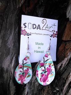 the earrings are made in hawaii with pink flowers on them, and one is hanging from a tree