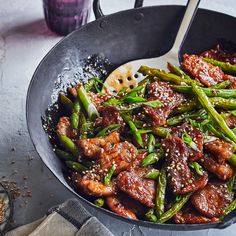 meat and asparagus stir fry in a skillet with sesame seeds on the side