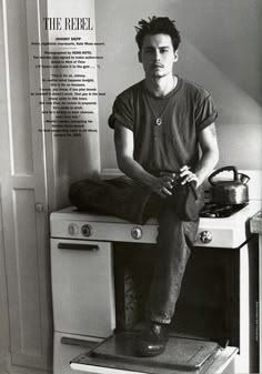 black and white photograph of a man sitting on top of an oven in a kitchen