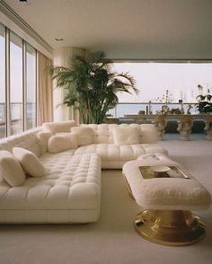 a living room filled with lots of white furniture and large windows overlooking the ocean in front of it