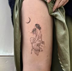 a woman with a small tattoo on her thigh holding a baby in her arms and the moon behind her