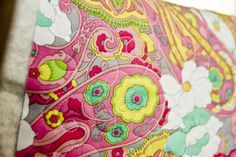 a pink and yellow floral print pillow on a bed with pillows in the back ground