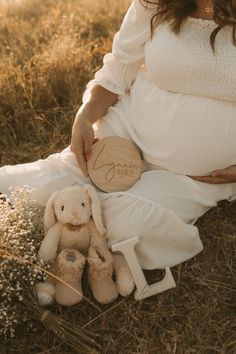 a pregnant woman sitting in the grass with her stuffed animal and name plate on it