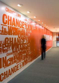 a man walking down a hallway next to a wall covered in orange and white words