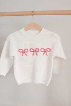 a white sweater with pink bows is hanging on a wooden hanger and it has the word hope written in red