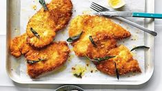 fried chicken on a tray with lemon wedges and herbs next to it, ready to be eaten