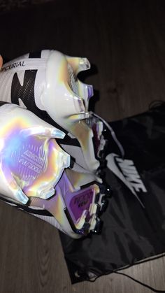 a person holding up a pair of white and purple soccer cleats on top of a wooden floor