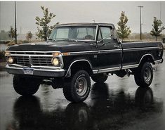 an old black pickup truck parked in a parking lot on a rainy day with no one around