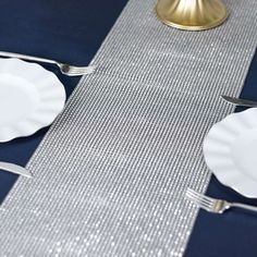 the table is set with white plates and silver place settings on blue linen, along with gold - plated napkins