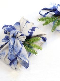 two blue and white napkins tied to each other with pine branches on top of them