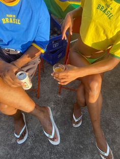 two people sitting next to each other holding drinks