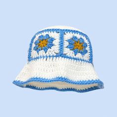 a white and blue crocheted hat with flowers on it's side, against a light blue background