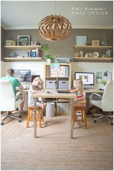 two people sitting at a desk in front of computer monitors and laptops with shelves above them