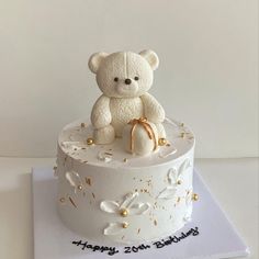 a white teddy bear sitting on top of a birthday cake with gold sprinkles