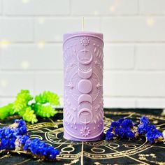 a purple candle sitting on top of a table next to blue flowers and greenery