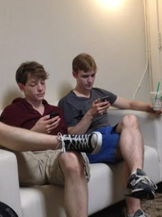 two boys sitting on a couch looking at their cell phones