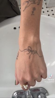 a woman's hand with a tattoo on her left arm and wrist, in front of a sink