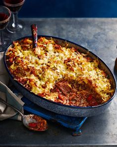 a casserole dish with meat, cheese and sauce in it next to two glasses of wine