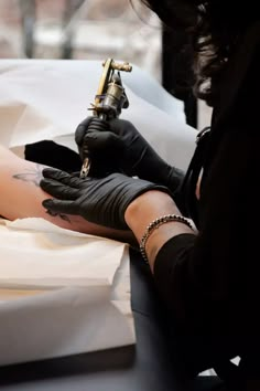 a woman with black gloves and tattoos on her arm holding a tattoo machine in one hand